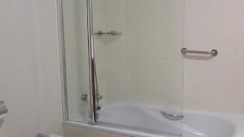 Een badkamer met een douche met glazen wand, een wit bad en een toilet.