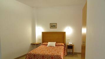 A bedroom with a wooden headboard, a patterned bedspread, two bedside tables, and a small bedside lamp.