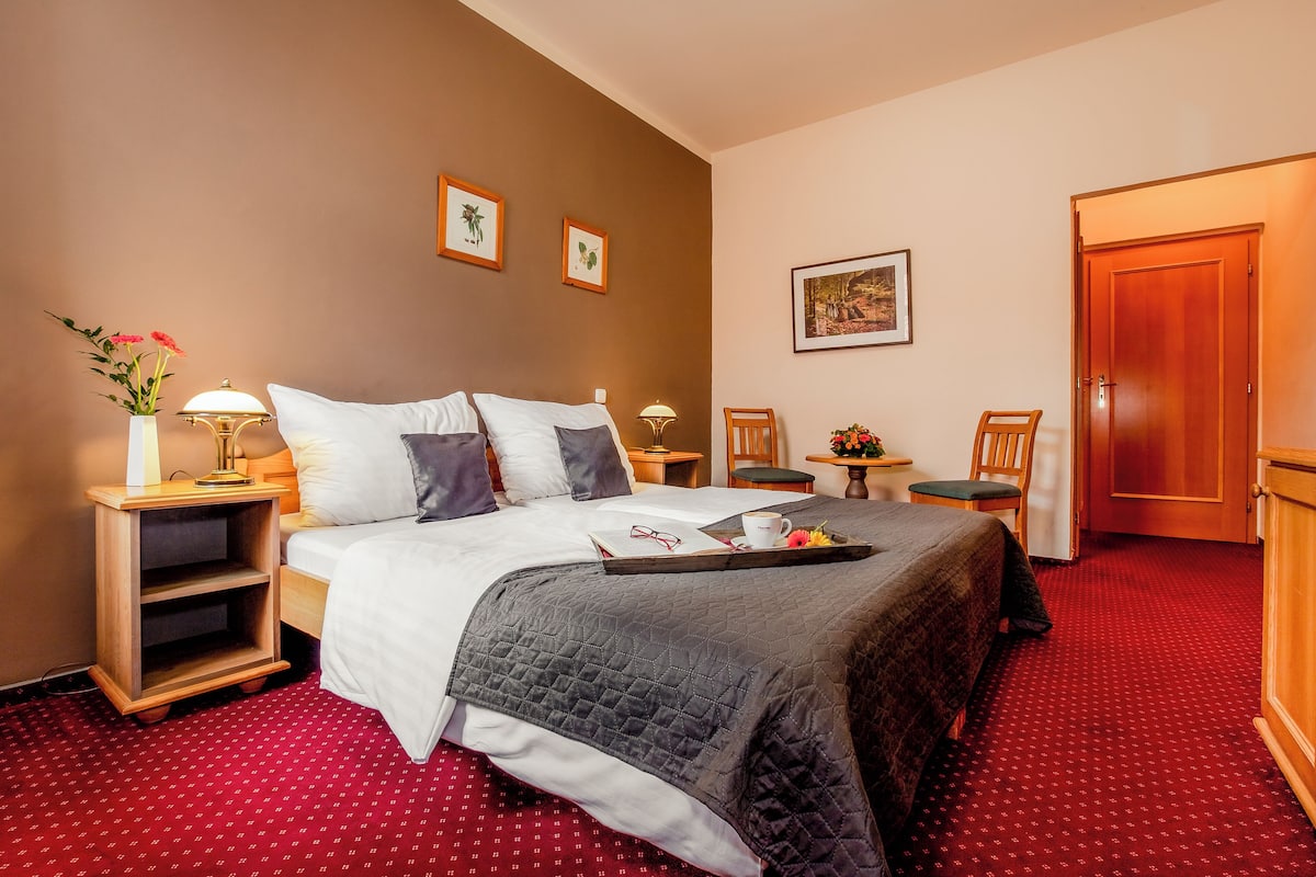 A neatly arranged hotel room with a bed, bedside tables, a chair, and a door.