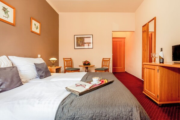 A hotel room with a bed, a wooden cabinet, a television, and a small table with a flower arrangement. - Hotel Panská (Bechyne)