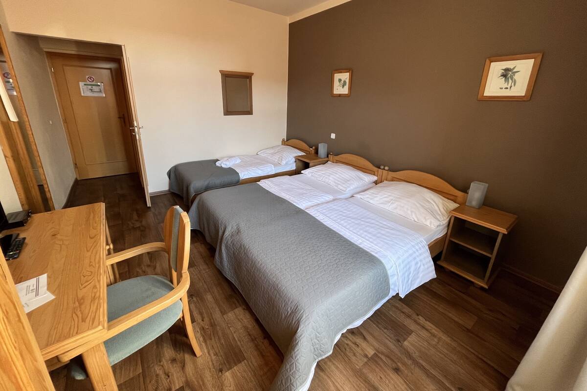 A hotel room with two beds, a desk, a chair, a small table, and a door.