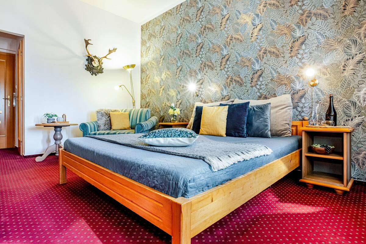 A bedroom with a wooden bed, patterned wallpaper, a small table, and a nightstand.