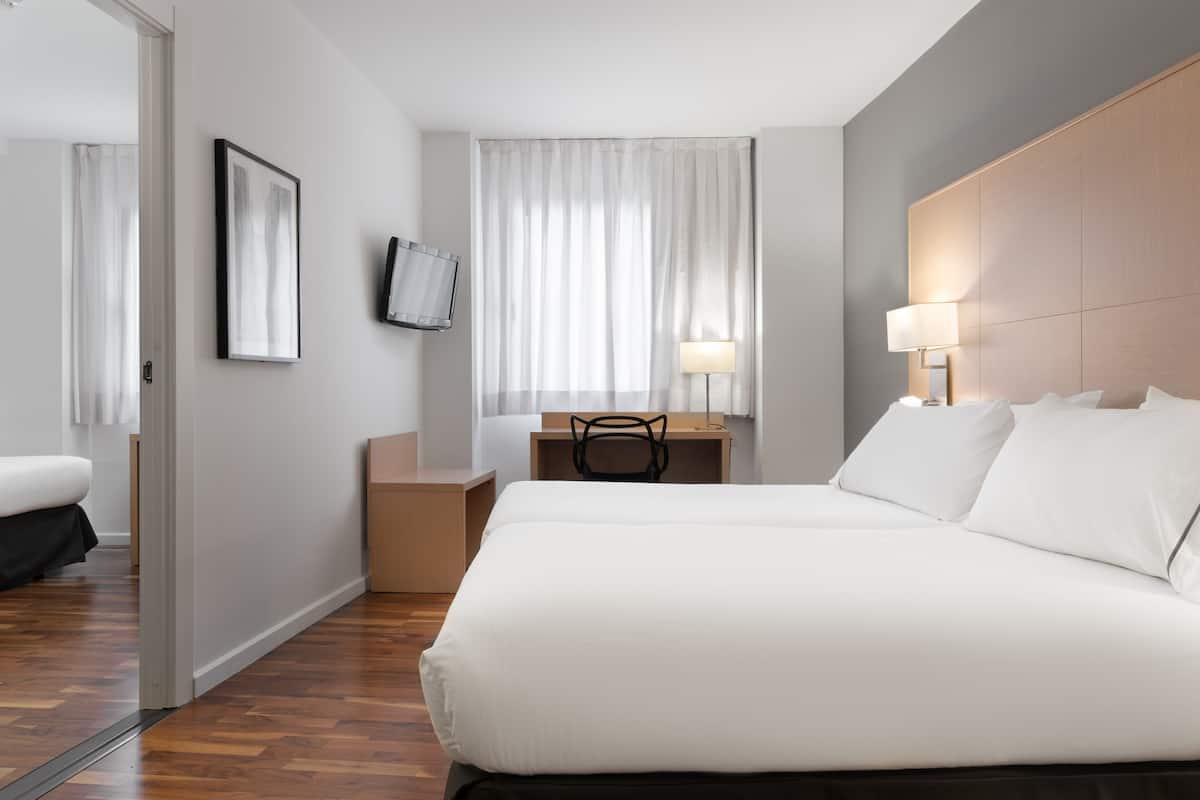 Hotelkamer met een groot bed, een bureau met stoel, een aan de muur bevestigde televisie en een raam met gordijnen.