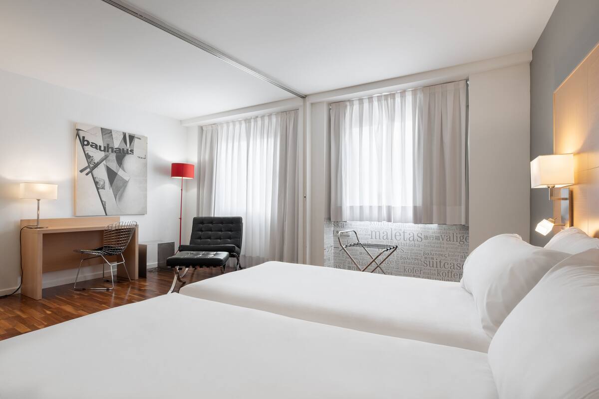 Een hotelkamer met twee bedden, een bureau, een stoel en een raam met gordijnen.
