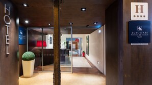 Un vestíbulo de hotel con suelo de madera, puerta de entrada de vidrio y una planta en maceta.