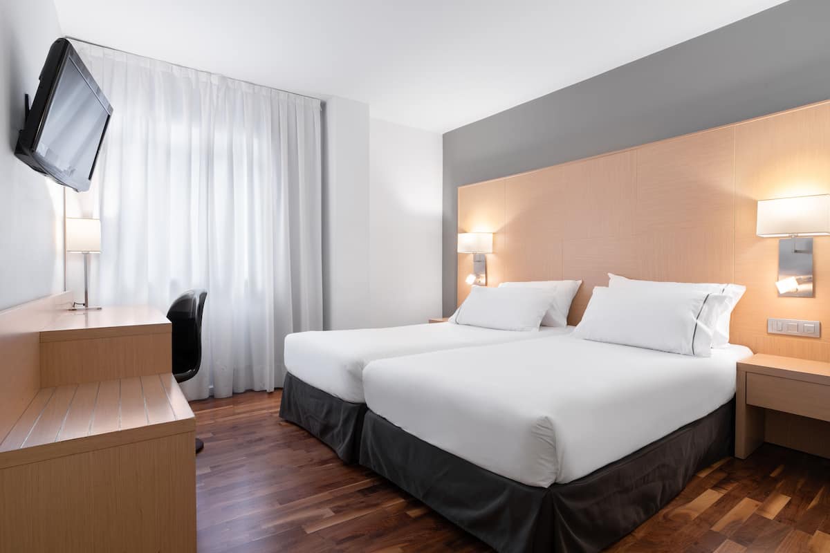 Een hotelkamer met twee bedden, een bureau, een aan de muur bevestigde televisie en twee bedlampjes.
