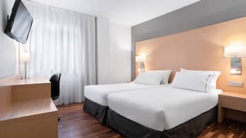 Ett hotellrum med två sängar, ett skrivbord, en TV som är monterad på väggen och två sänglampor.