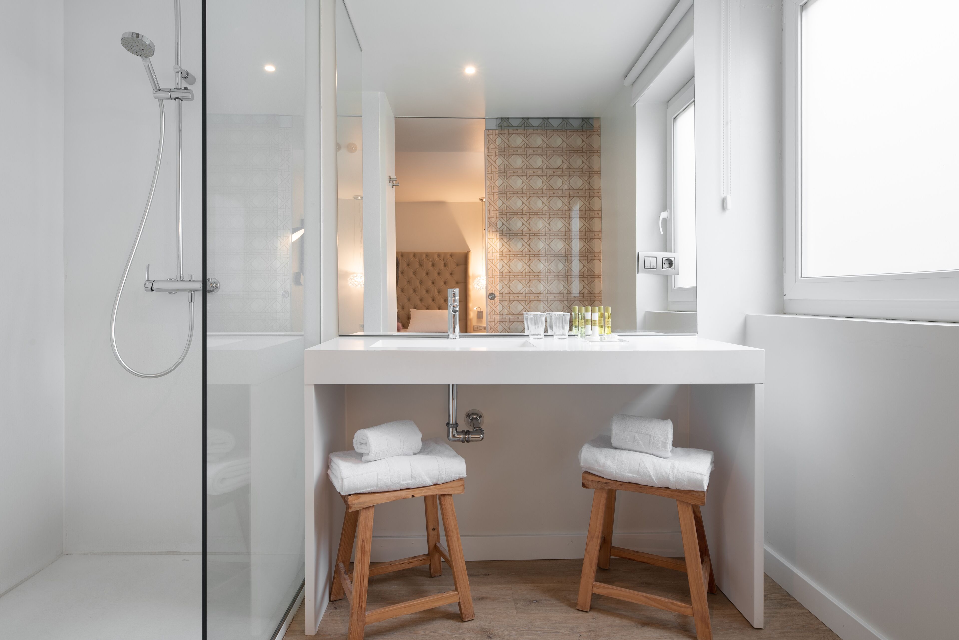 A modern bathroom with a glass-enclosed shower, a white vanity with two stools, and a large mirror.