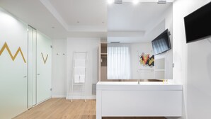 Un baño moderno y minimalista con un tocador blanco, un espejo grande y un televisor montado.