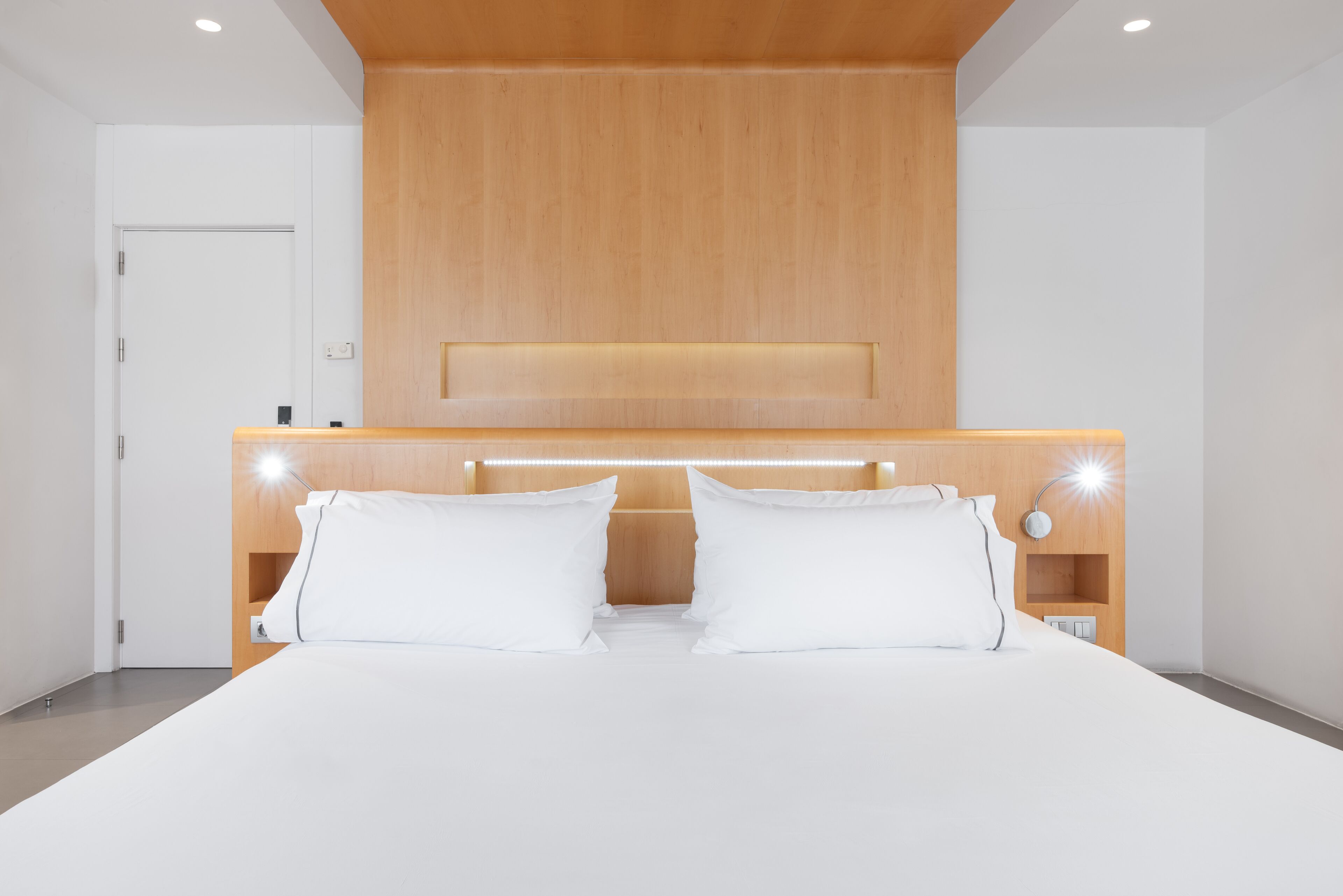 Una habitación de hotel moderna con cabecera de madera, ropa de cama blanca y lámparas de noche.