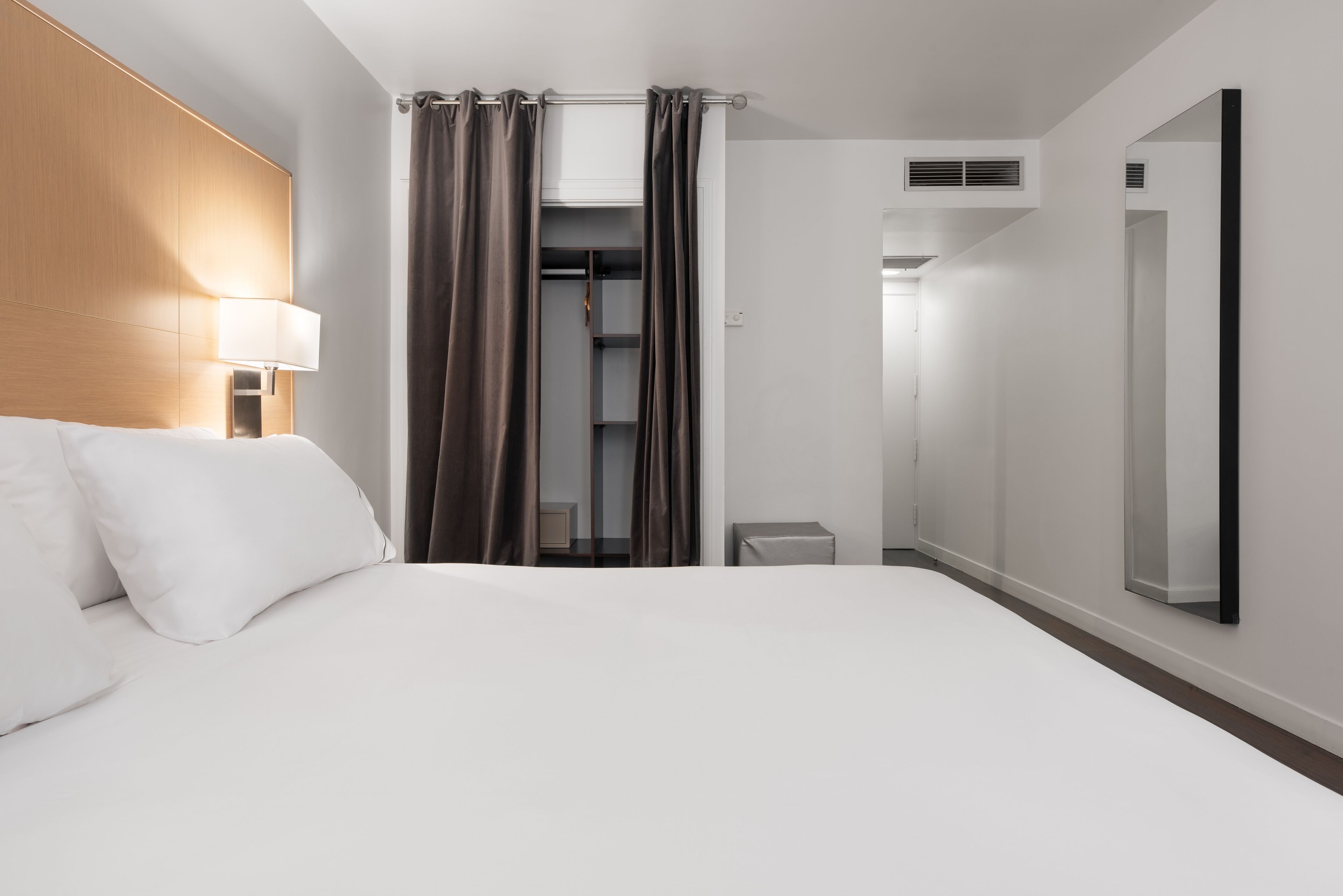 Una habitación de hotel con cama, lámpara de noche, armario, espejo y una pequeña mesa.