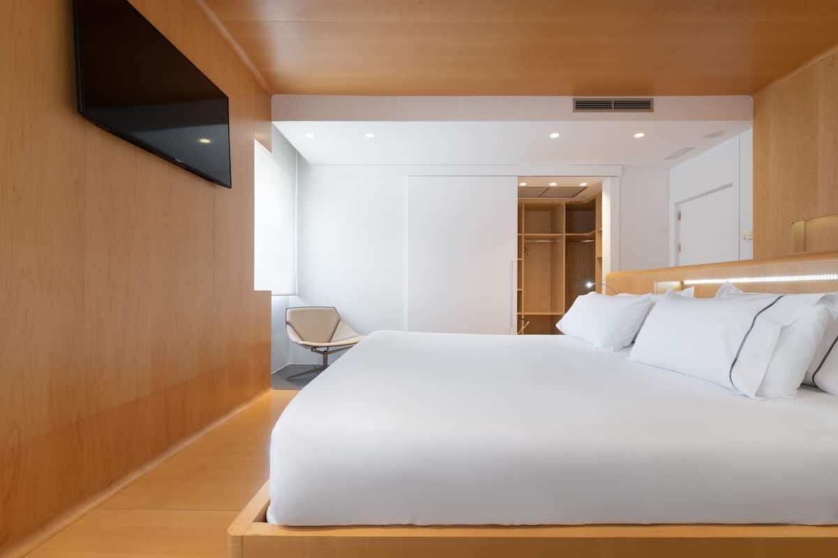 Een moderne slaapkamer met een groot bed, een fauteuil en een inloopkast.