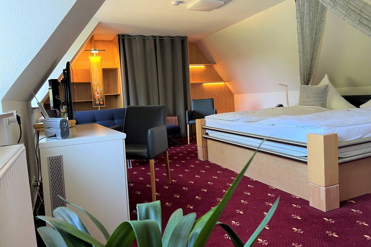 Una habitación de hotel con cama, escritorio, computadora, una silla y una planta.