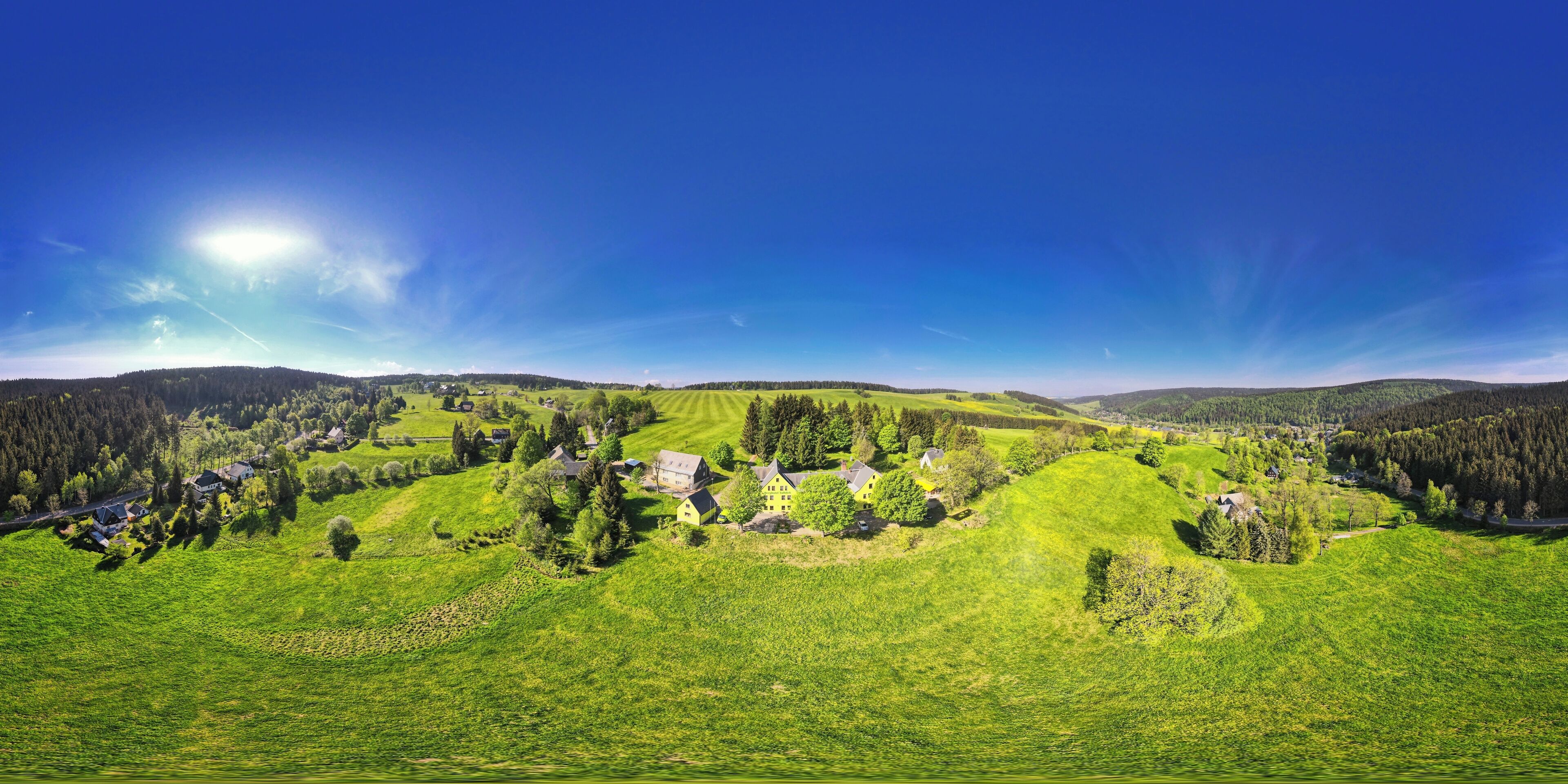Panoramica di un paesaggio rurale con dolci colline, case sparse e fitti boschi.