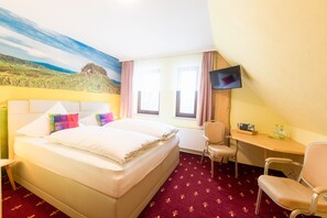 A hotel room with a bed, a desk, a chair, a TV, and a window with curtains. - Berghotel Talblick (Rechenberg-Bienenmuehle)