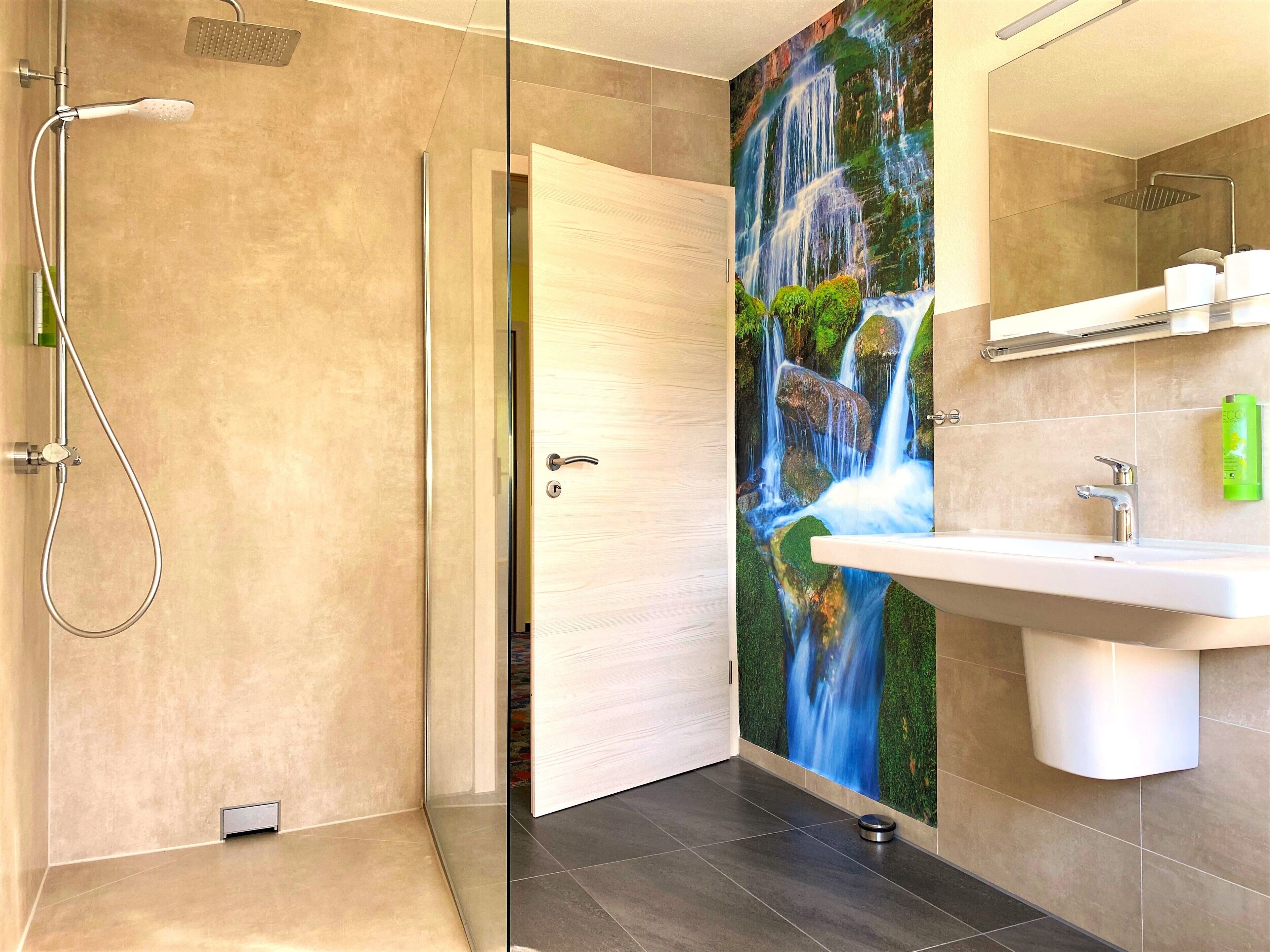 A modern bathroom with a shower, a sink, and a decorative waterfall mural.