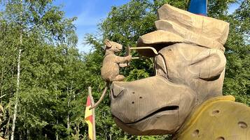 A wooden sculpture of a horse's head with a rider, set against a backdrop of trees and a flag.