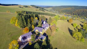Vista aérea de una extensa propiedad con varias construcciones, rodeada de colinas onduladas y densos bosques.