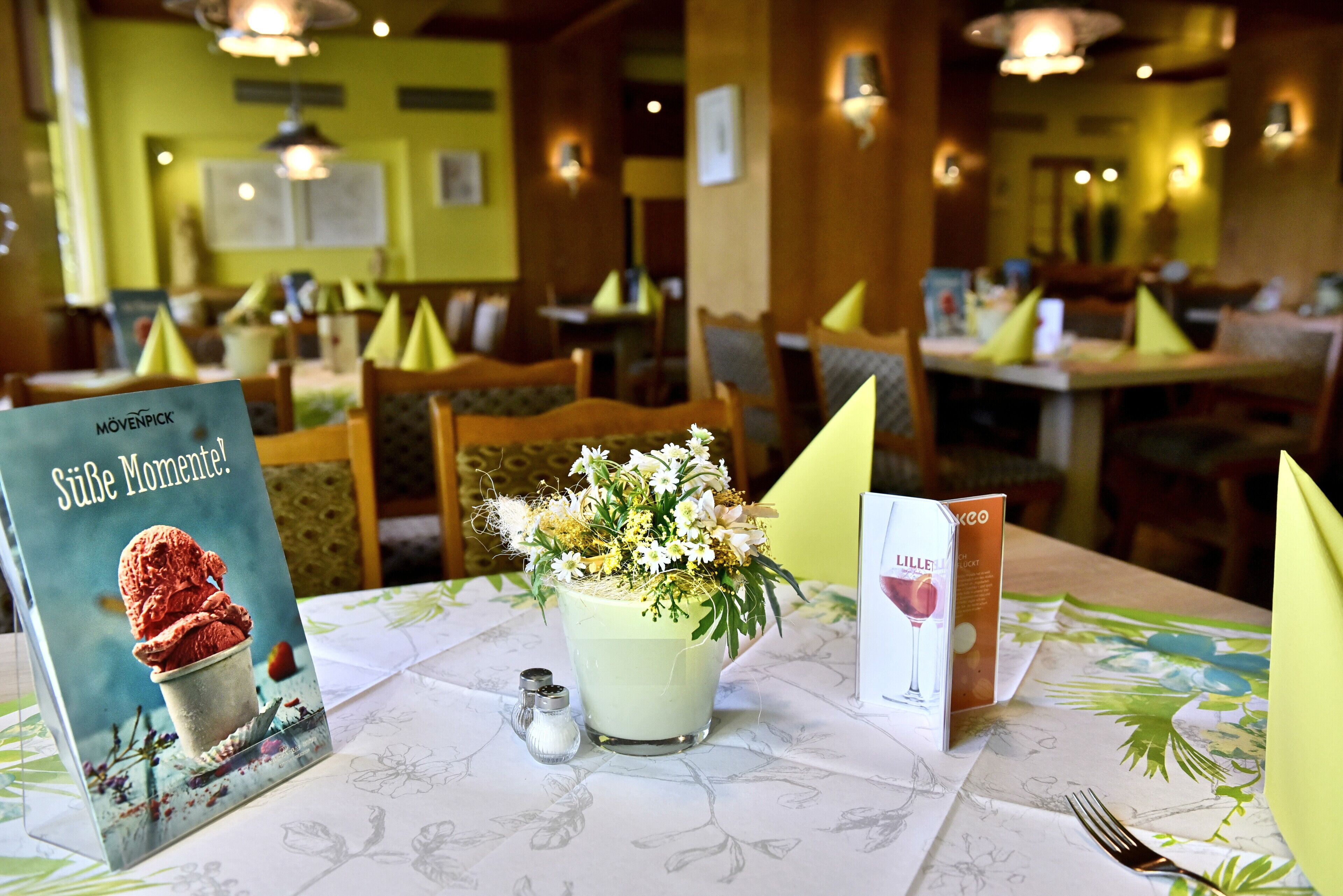 Un ambiente de restaurante con mesas listas para comer, un menú y un arreglo floral decorativo.