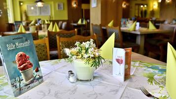 Un ambiente de restaurante con mesas listas para comer, un menú y un arreglo floral decorativo.