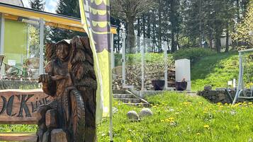 A wooden sculpture of a figure holding a staff, a yellow flag, and a sign with the word "LOCK" in a garden setting.