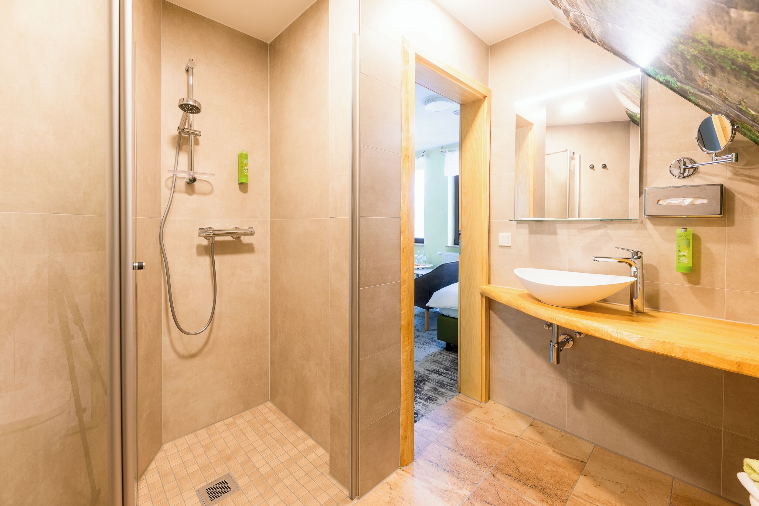 Un baño moderno con ducha envuelta en vidrio, tocador de madera con lavabo tipo recipiente y un espejo grande.