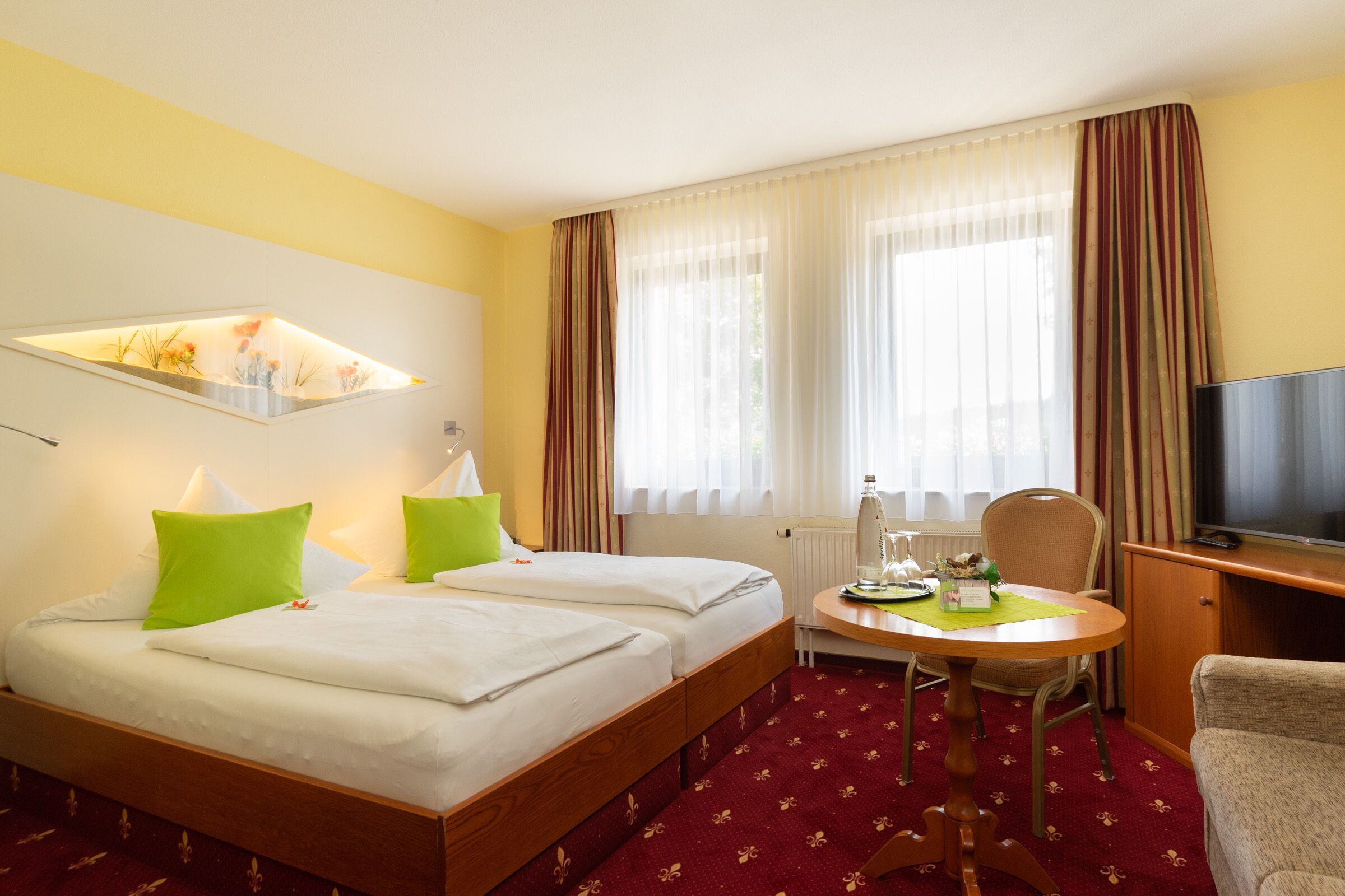 A hotel room with two beds, a television, a table with a chair, and a window with curtains.