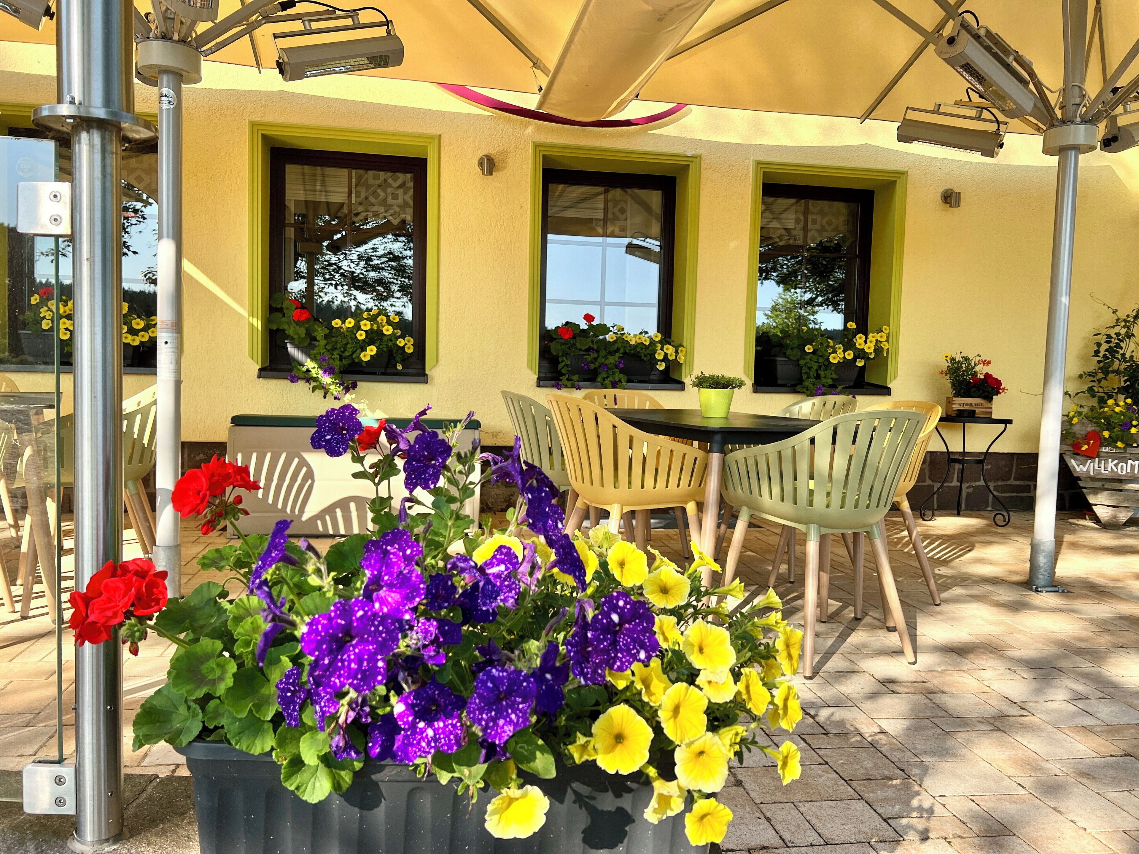 An outdoor patio with a table and chairs, surrounded by potted plants and flowers.
