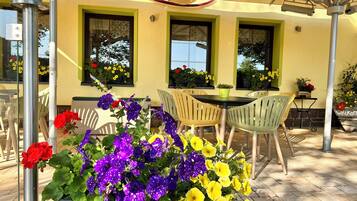 An outdoor patio with a table and chairs, surrounded by potted plants and flowers.