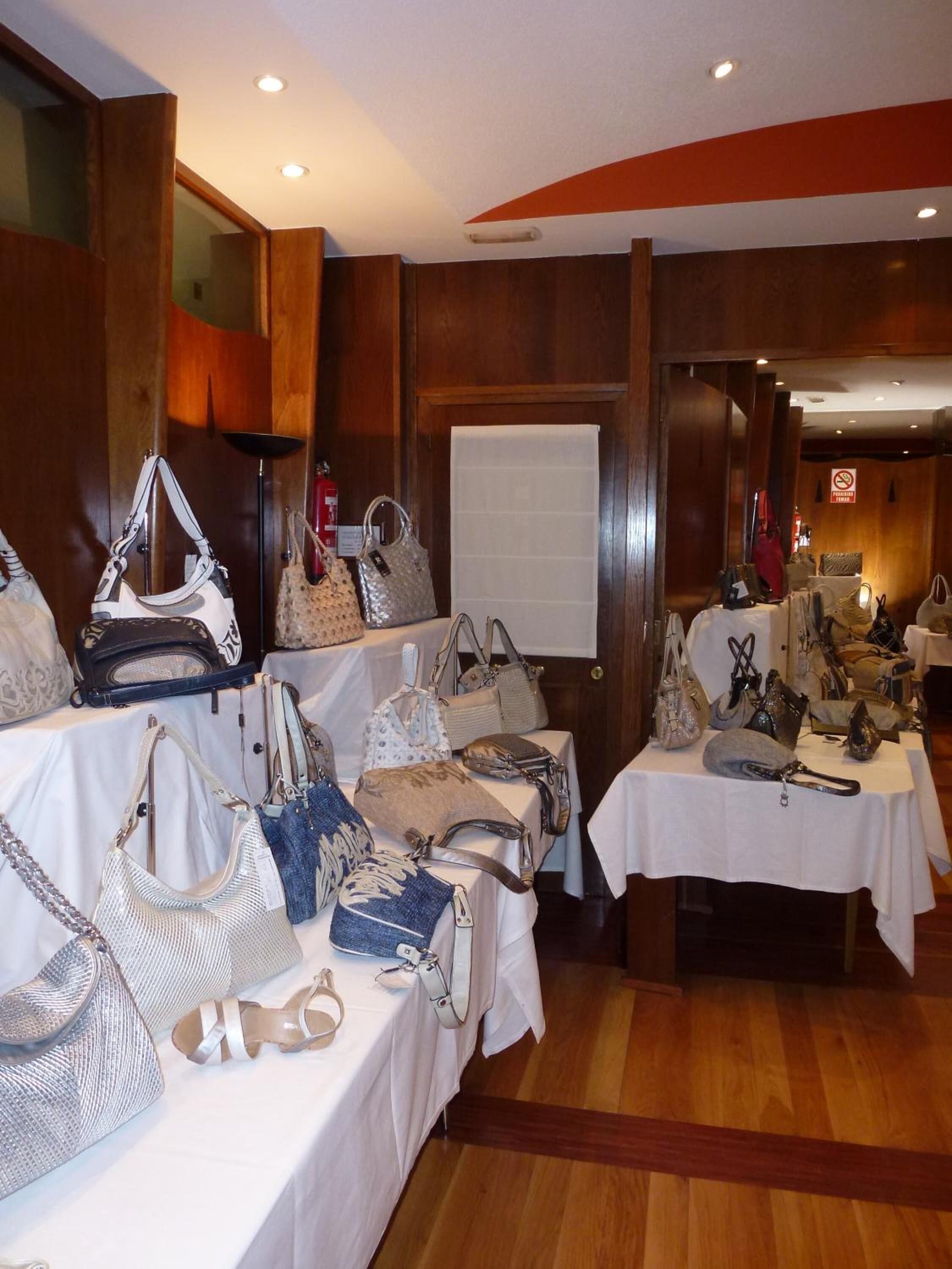 A display of handbags on tables in a room with wooden paneling and a whiteboard.