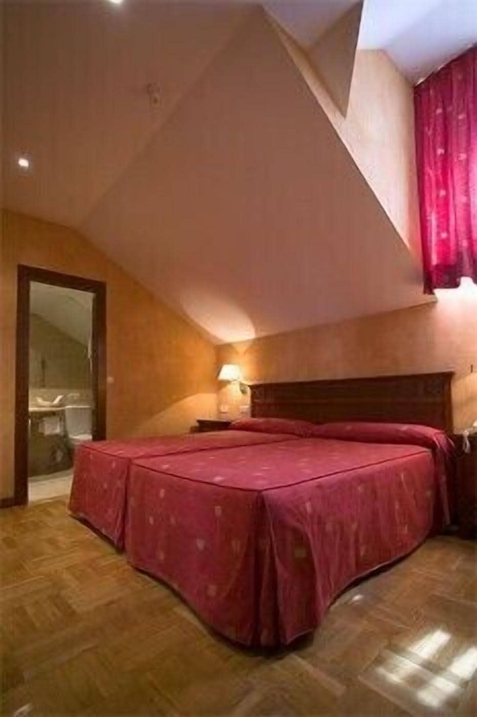 A bedroom with a large bed, wooden flooring, a wooden headboard, a nightstand, and a window with curtains.