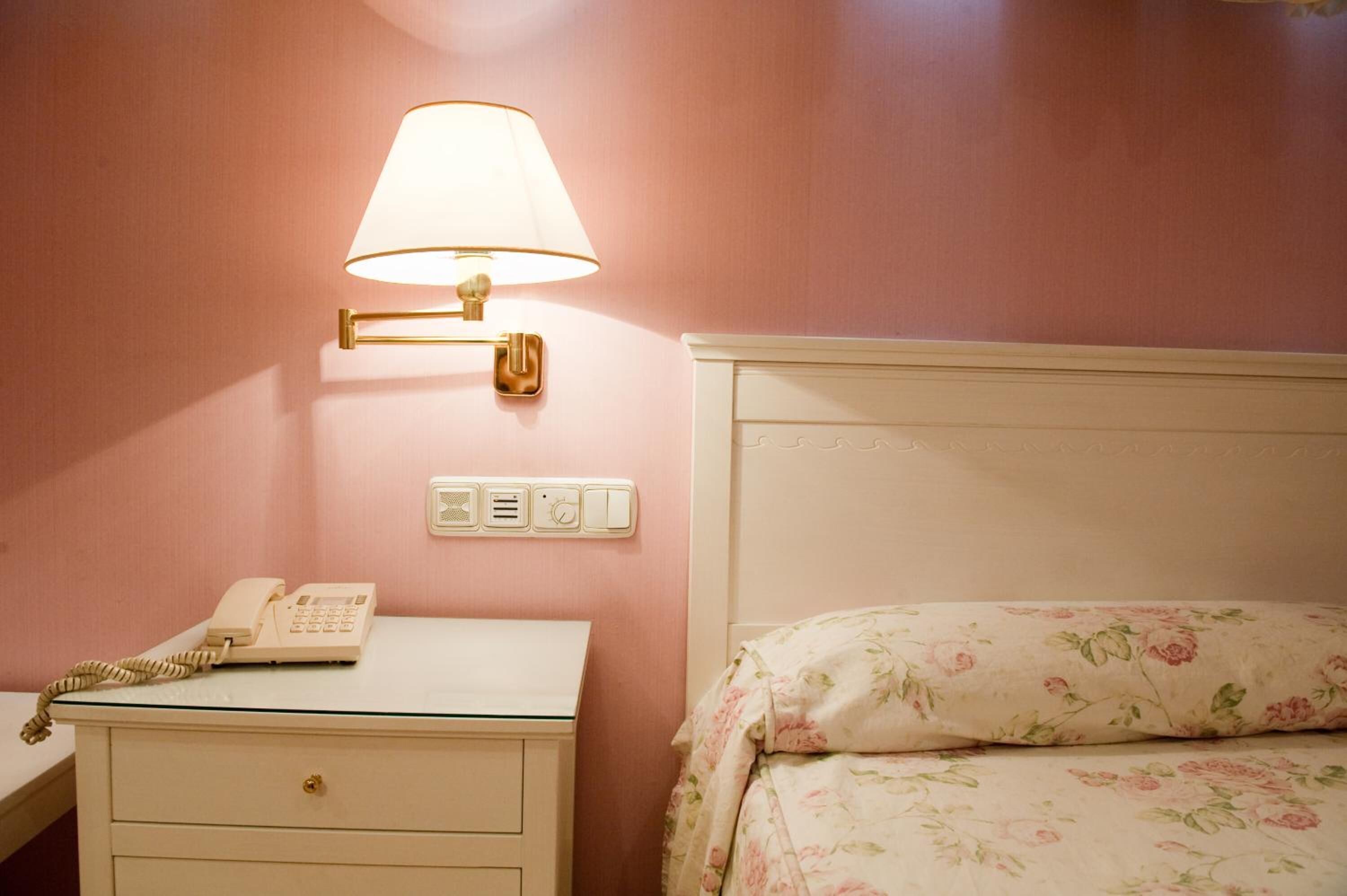 A hotel room with a bedside table, a lamp, a telephone, and a bed with floral bedding.
