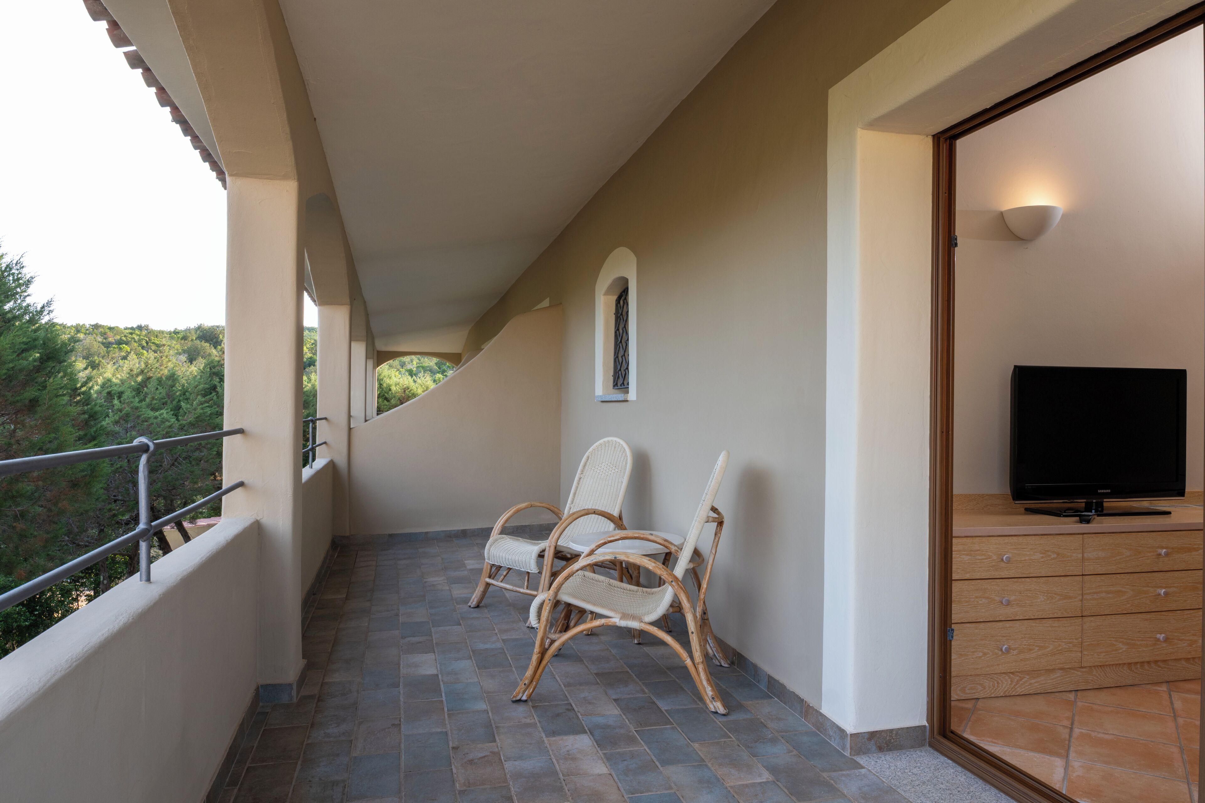 Un balcon avec des fauteuils en osier, un téléviseur et une commode en bois.
