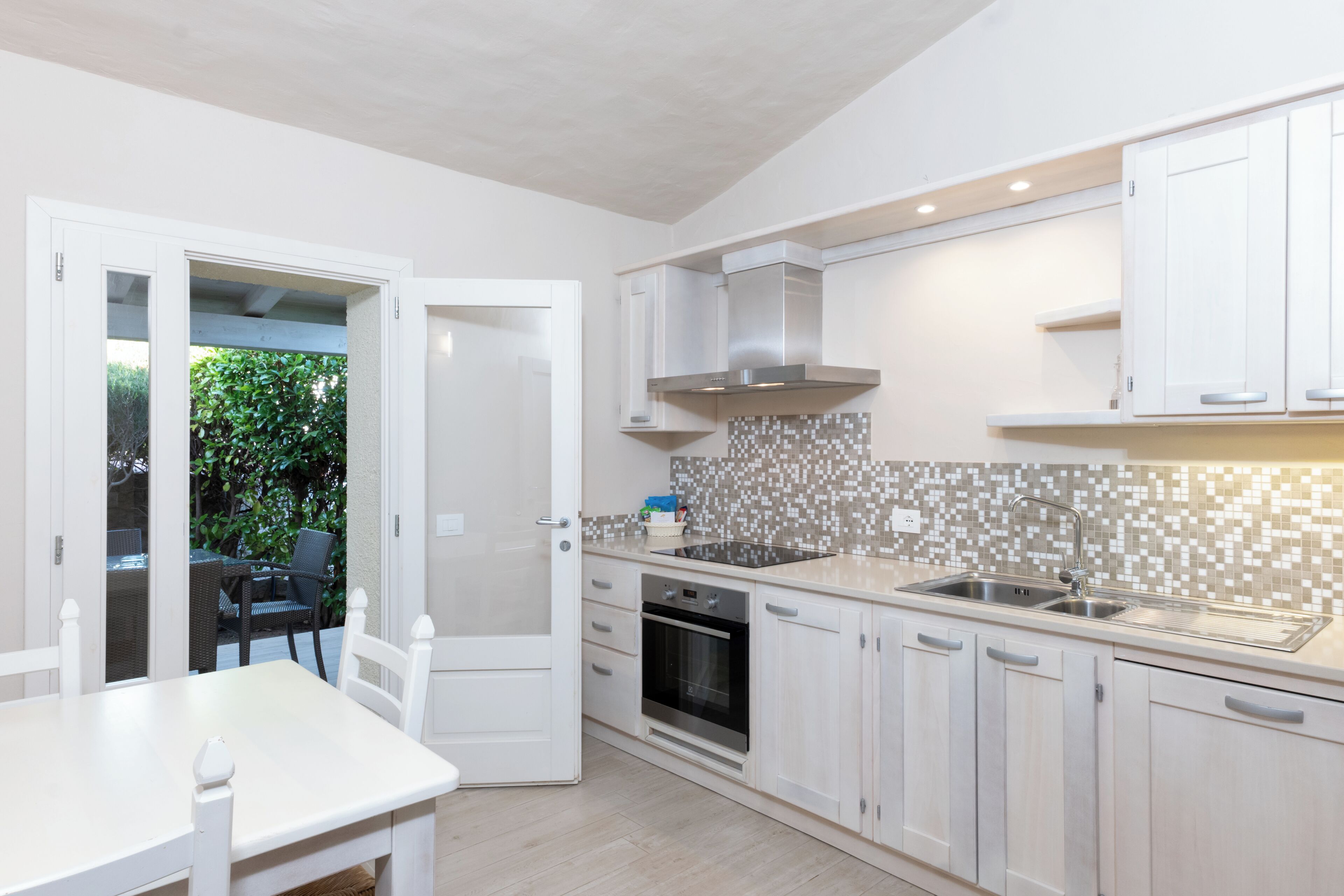 Une cuisine moderne avec des meubles blancs, un pare-feu en carreaux et un coin repas comprenant une table et des chaises.