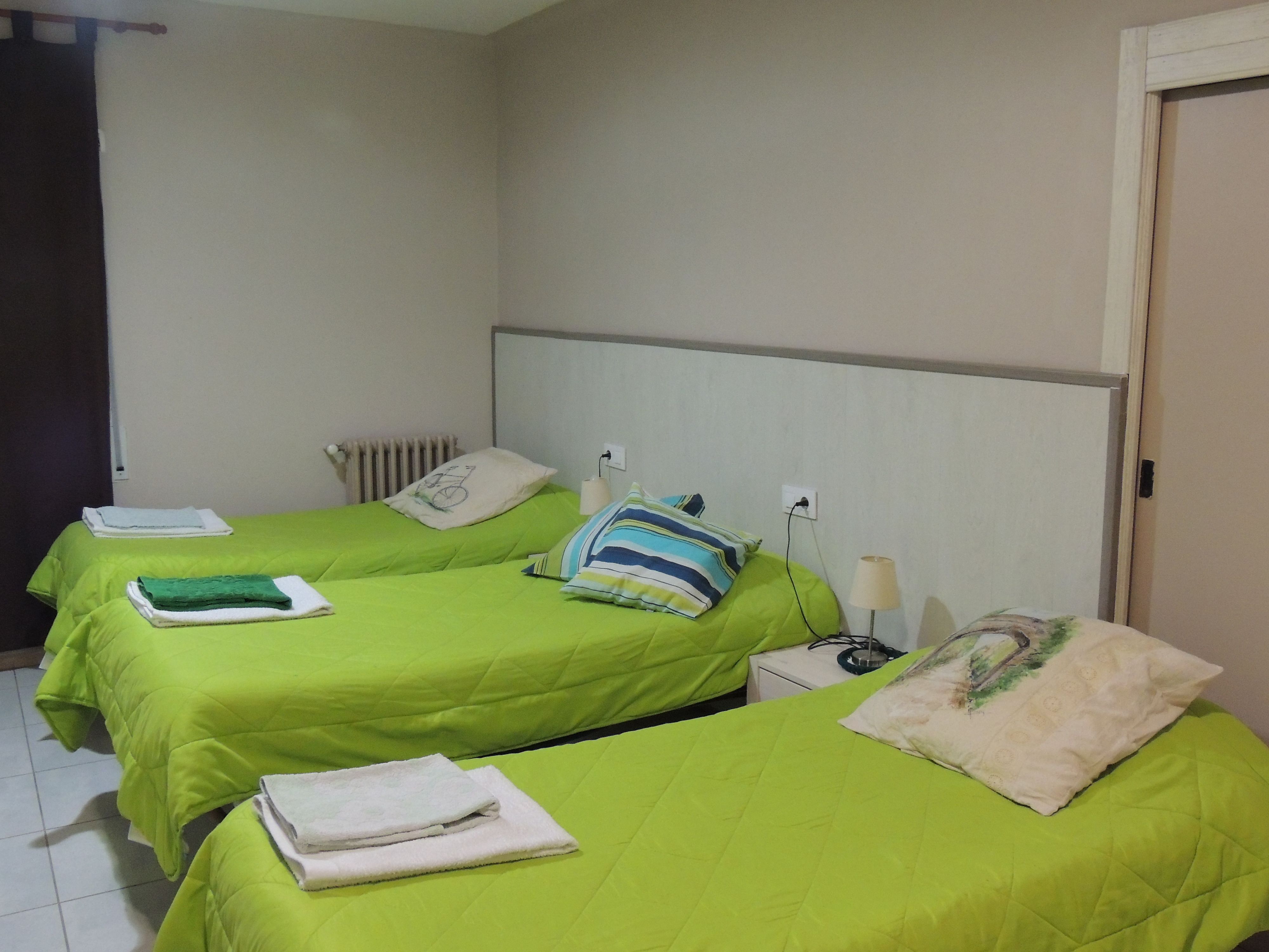 Une chambre d’hôtel avec deux lits, chacun doté de draps et d’oreillers verts, une table de chevet avec une lampe et un radiateur fixé au mur.