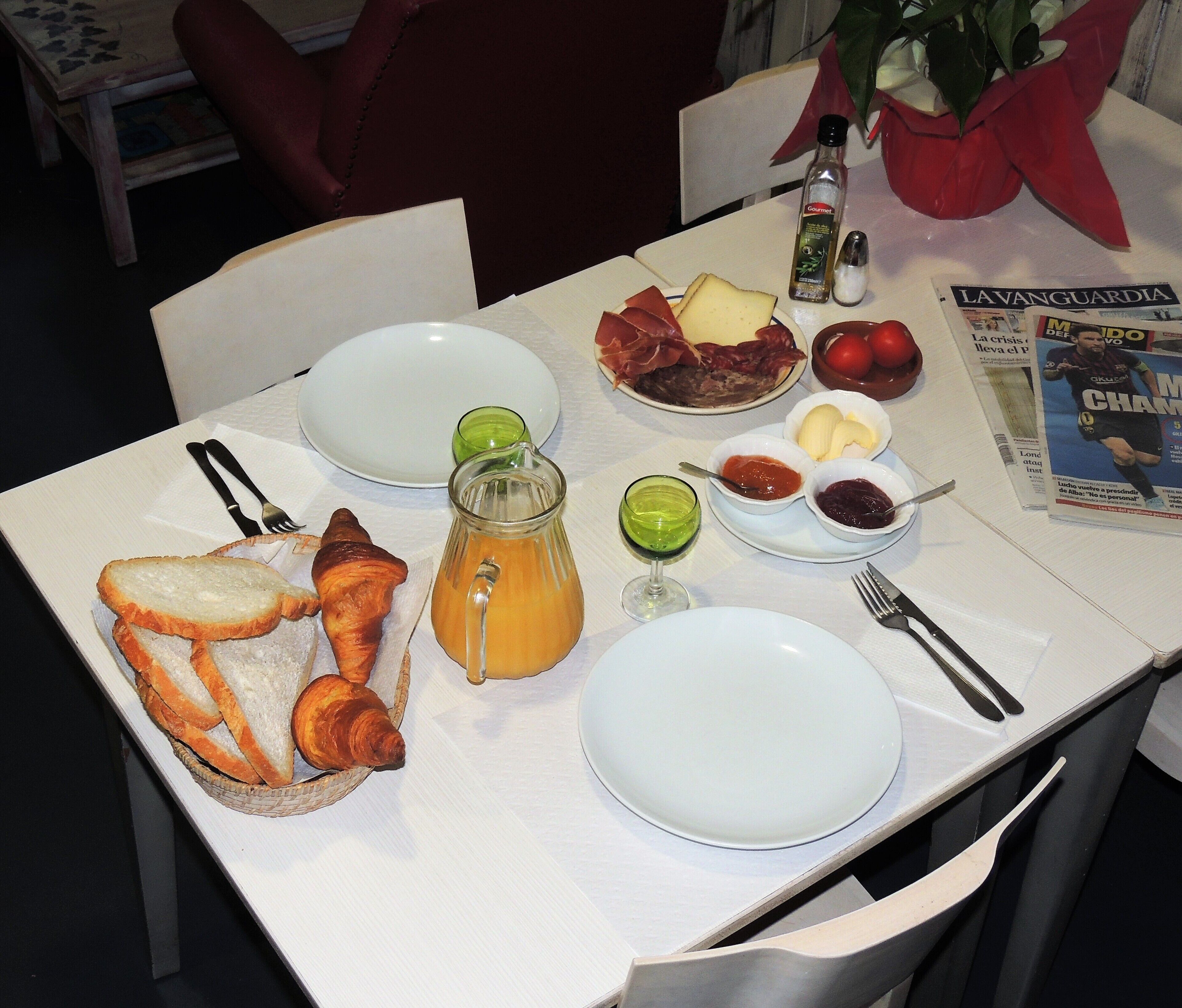 Ein Frühstückstisch mit Tellern, Brot, Croissants, einem Saftkrug und Gewürzen.