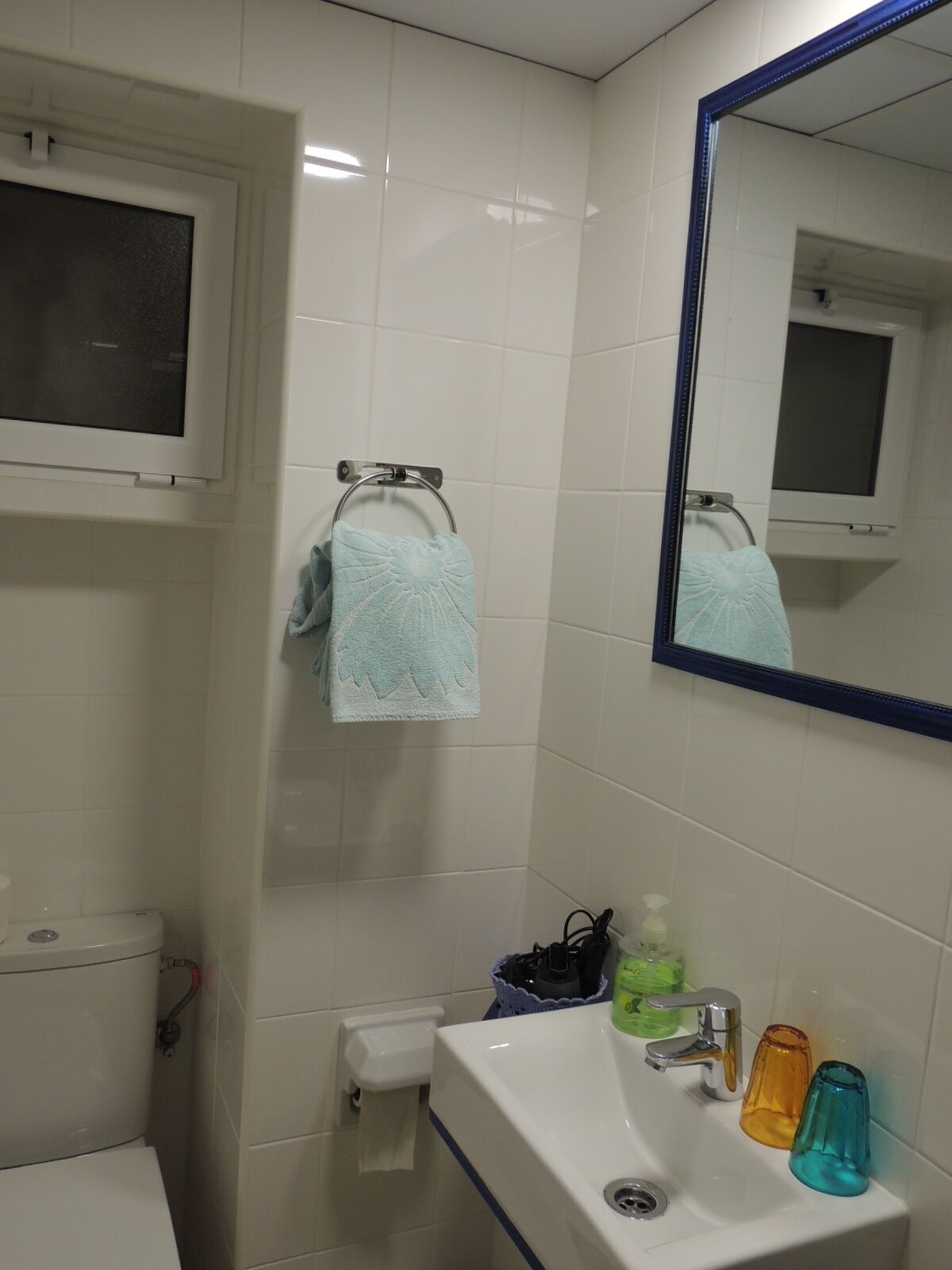Un baño con inodoro, lavamanos, espejo y toallero.