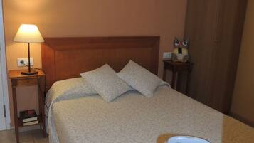 A hotel room with a bed, a nightstand with a lamp, a wooden wardrobe, and a suitcase.