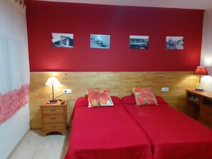 A room with two beds, a wooden headboard, a red wall, and four framed pictures. - Can Massot (Angles)