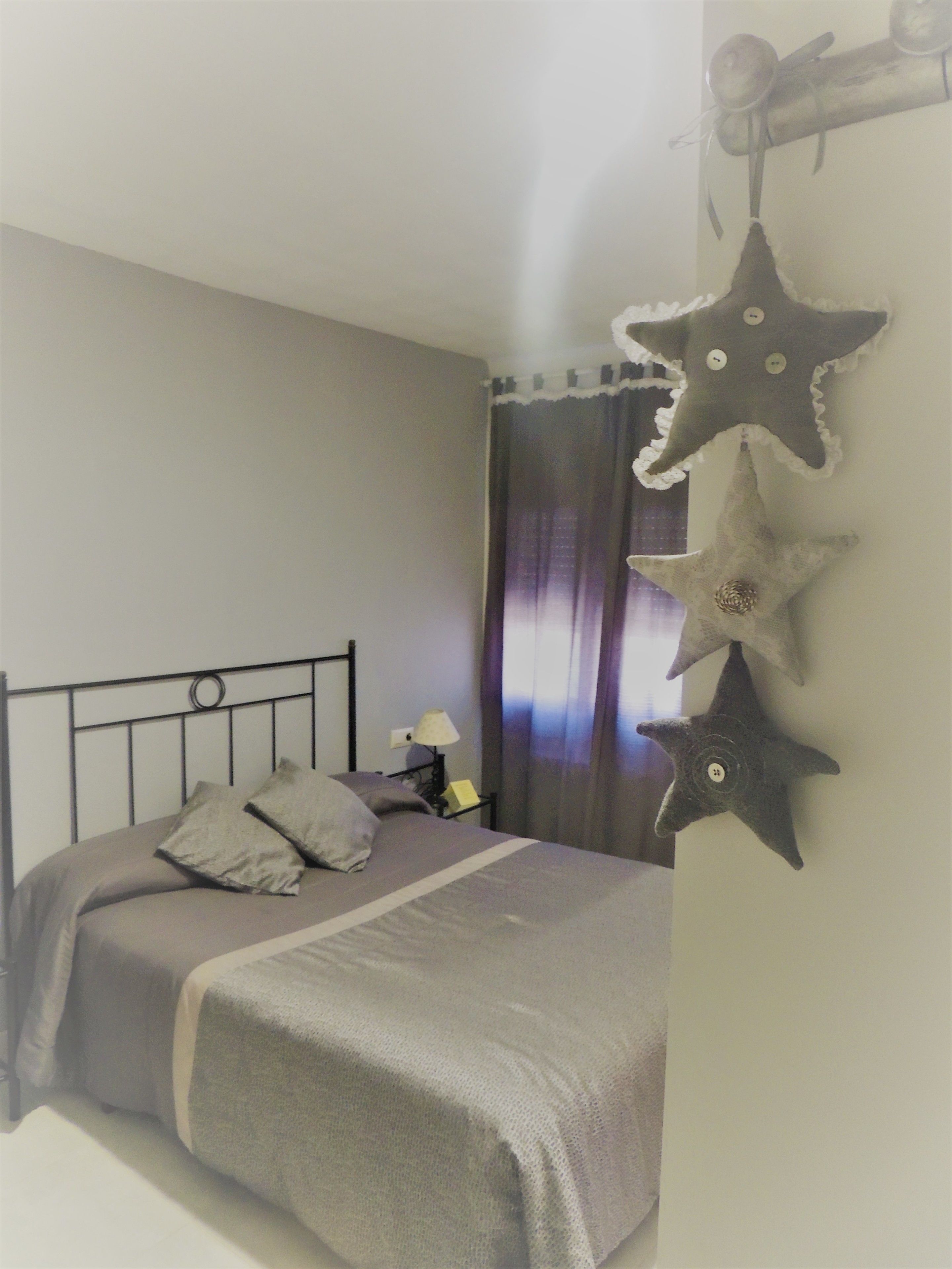Un lit bien fait, avec des oreillers, une table de chevet avec une lampe et des décorations en forme d’étoiles sur le mur.