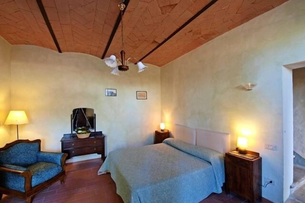 Un dormitorio con cama, una silla, cómoda y mesita de noche con lámparas.