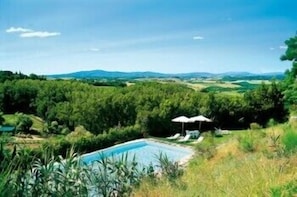 Une piscine entourée d’une végétation luxuriante, avec des collines en arrière-plan.