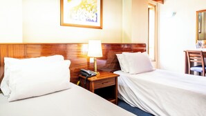 A hotel room with two beds, a bedside table with a lamp, a telephone, and a framed picture on the wall.