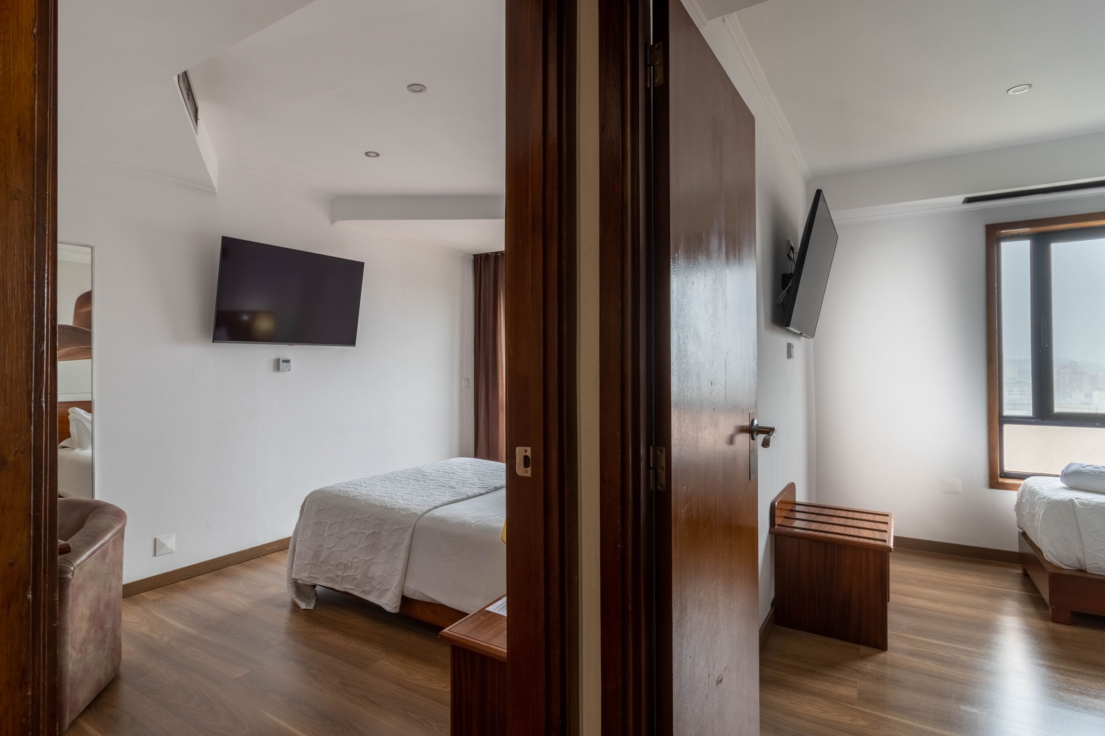 Une chambre à coucher moderne, avec un lit, un téléviseur fixé au mur et une fenêtre laissant entrer la lumière naturelle.