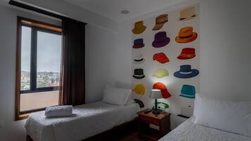 Habitación de hotel con dos camas, un ventanal grande y una pared decorada con varios sombreros.