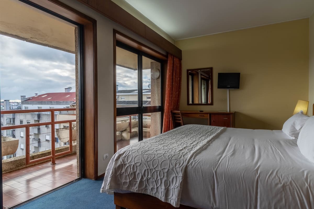 A hotel room with a large bed, a television, and a balcony with a view of the city.