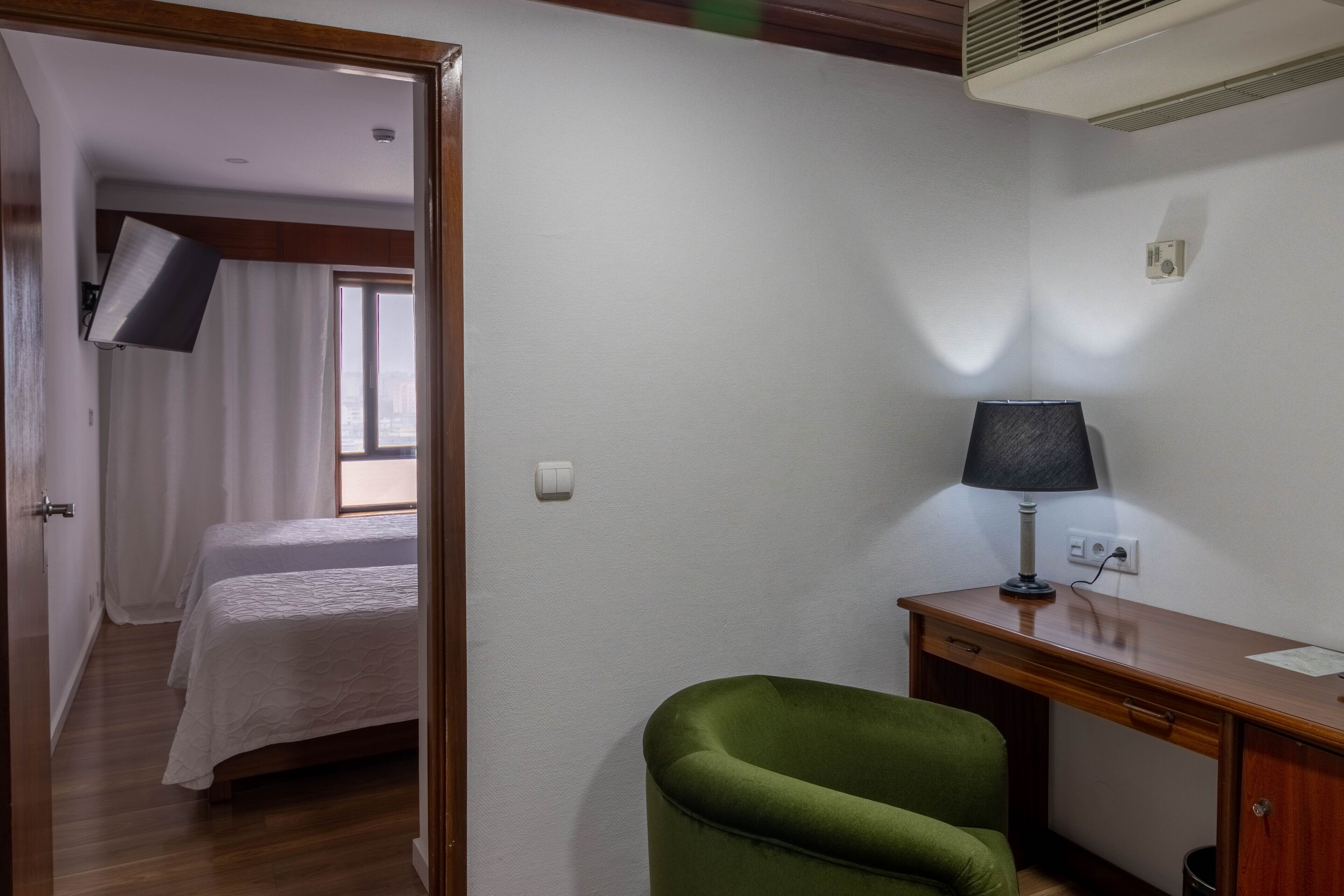 Une chambre avec un lit, un bureau, une chaise et un téléviseur fixé au mur.