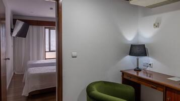 Une chambre avec un lit, un bureau, une chaise et un téléviseur fixé au mur.