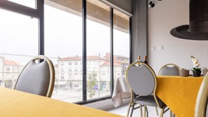 A dining area with a yellow table, grey chairs, and a view of buildings through large windows. - AS São João da Madeira (Sao Joao da Madeira)