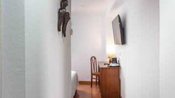 Een kleine kamer met een bed, een houten bureau, een stoel en een wandtelevisie.